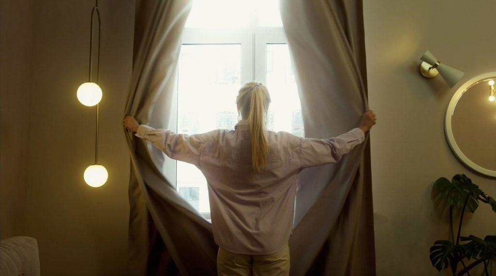 Woman opening up curtains to let the light in. 